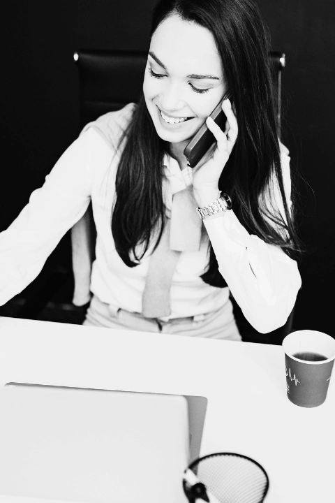 Business professional speaking on a phone while working at a desk with a laptop.